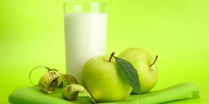 Glass of kefir, apples and measuring tape, on green background